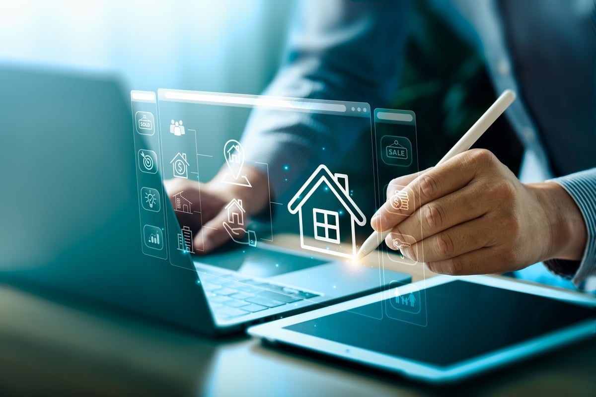 A man in a suit with a tablet, laptop, and real estate icons