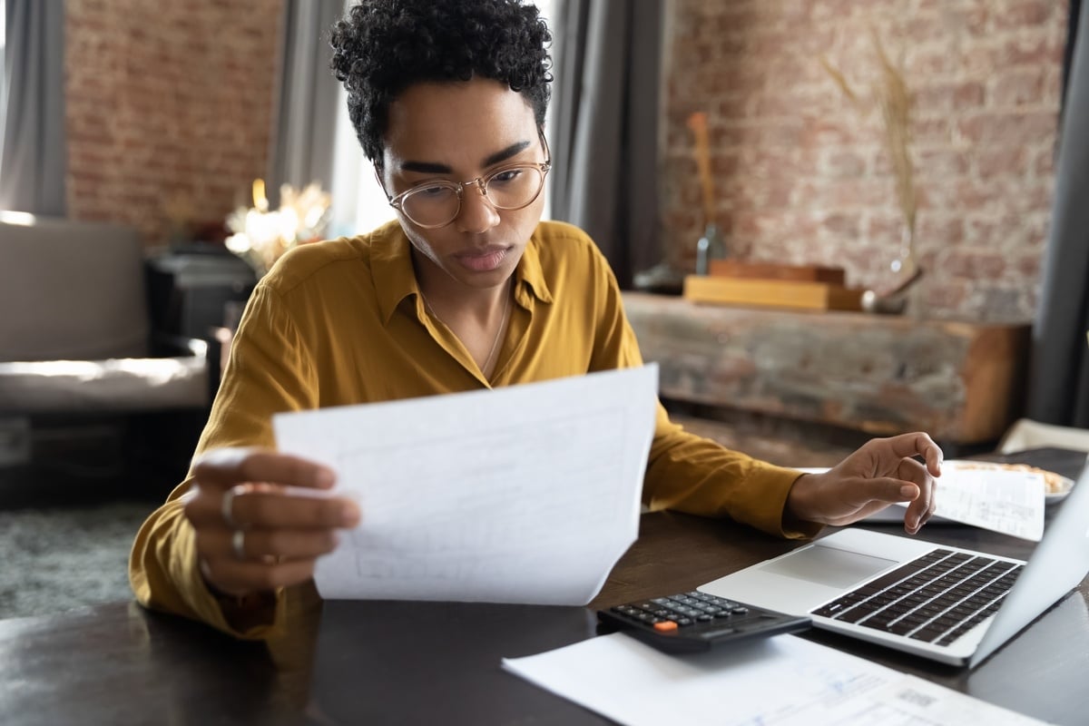 A woman looking at a document and typing on a laptop