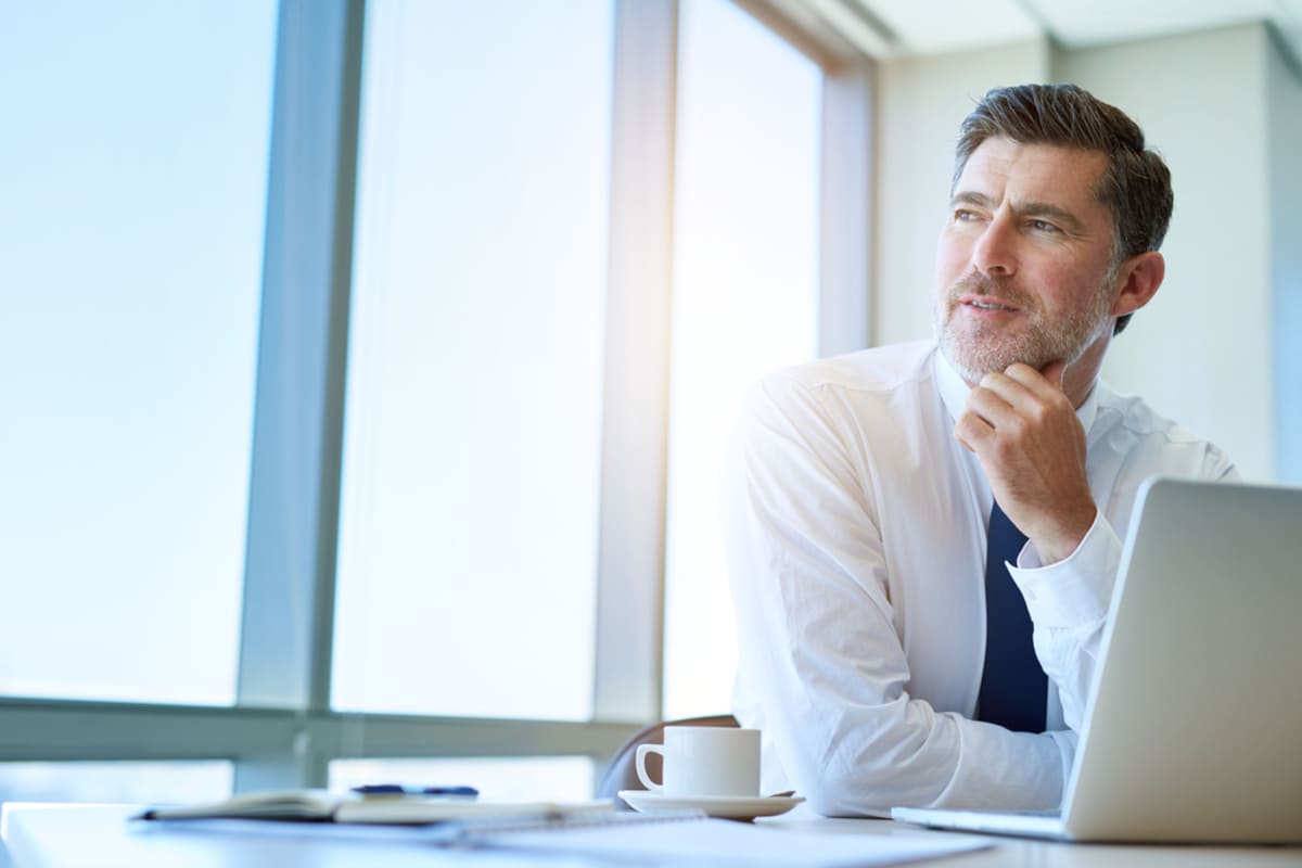 Businessman in front of laptop with hand in chin signaling to be thinking