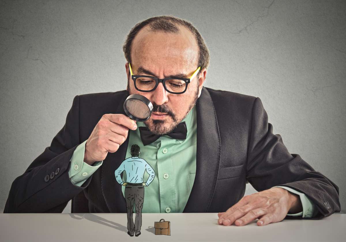 Curious corporate businessman skeptically meeting looking at small employee standing on table through magnifying glass