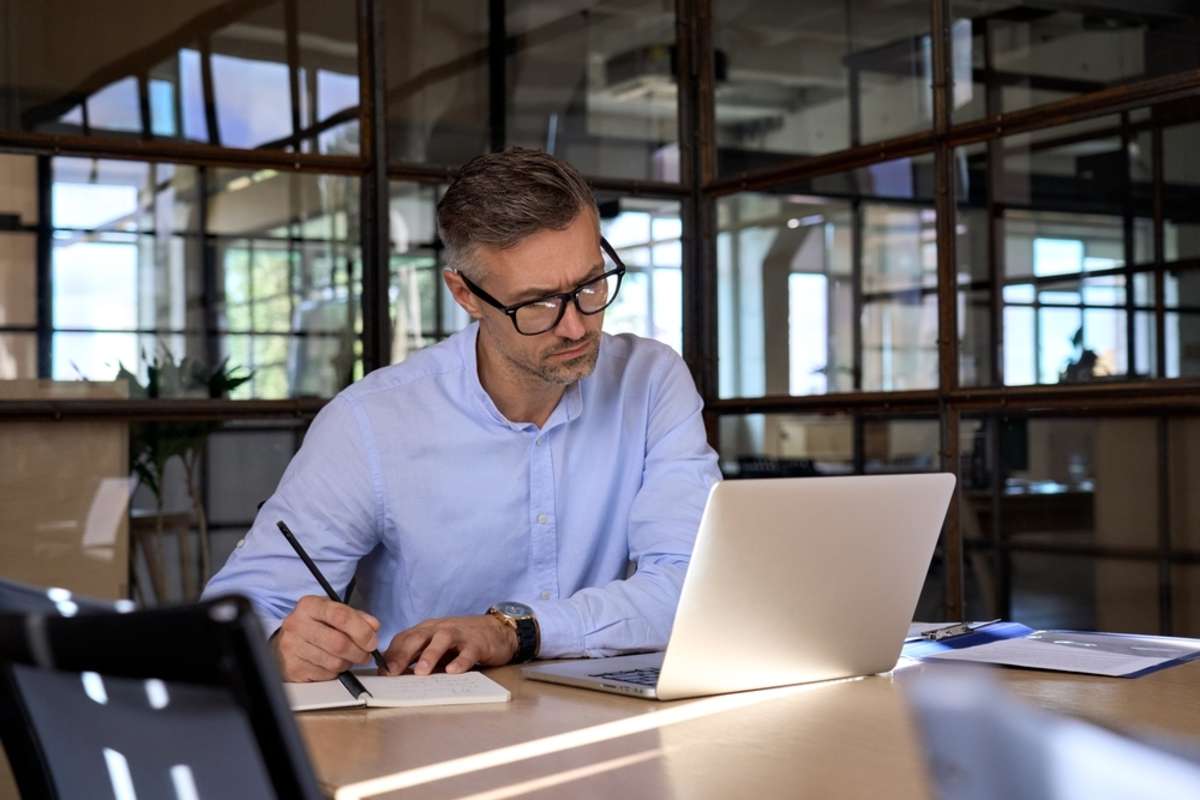 Mature business man executive manager looking at laptop computer watching online webinar training or having virtual meeting video conference taking notes