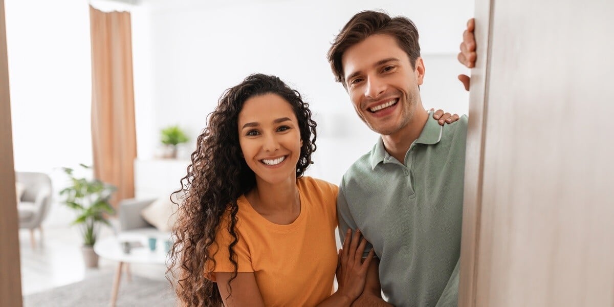 Portrait of excited cheerful couple inviting guest friends to enter their home