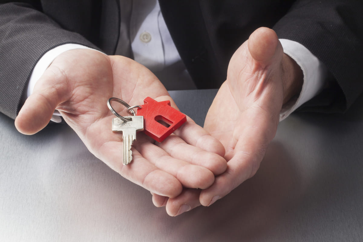 Property manager with key in hands, keyholder is a red model house.